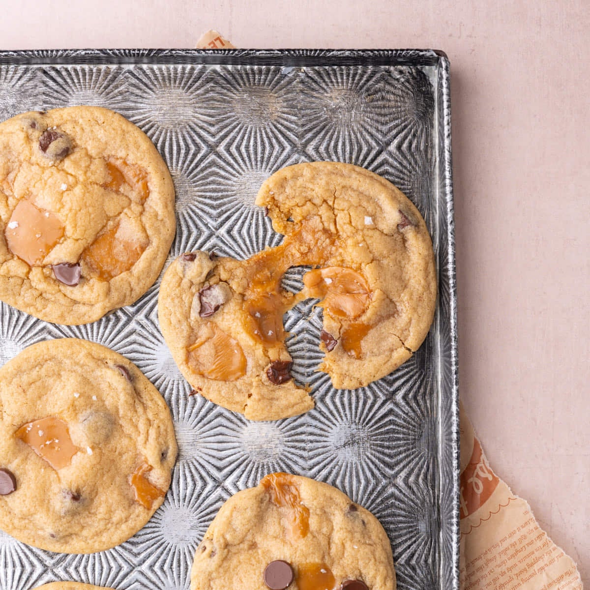 Close up of chocolate chip caramel cookie split in half and pulled apart to show the gooey caramel.