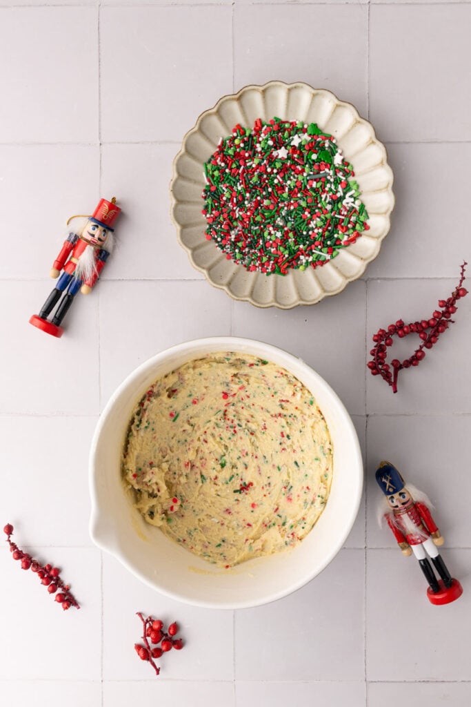 Half of the Christmas sprinkles for the recipe added to the cookie dough and the other half added to a shallow bowl to dunk the cookies in.