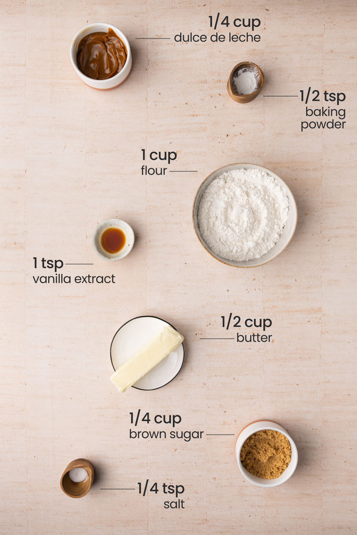 Overhead view of the ingriedients for Dulce de leche Cookies - baking powder, flour, vanilla extract, butter, brown sugar, salt, and dulce de leche.