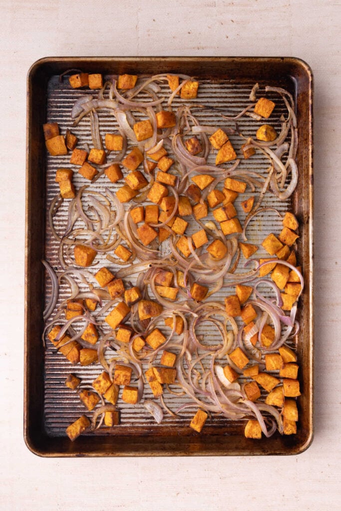 Adding sliced red onion to a sheet pan with almost-ready sweet potato to roast in the oven.
