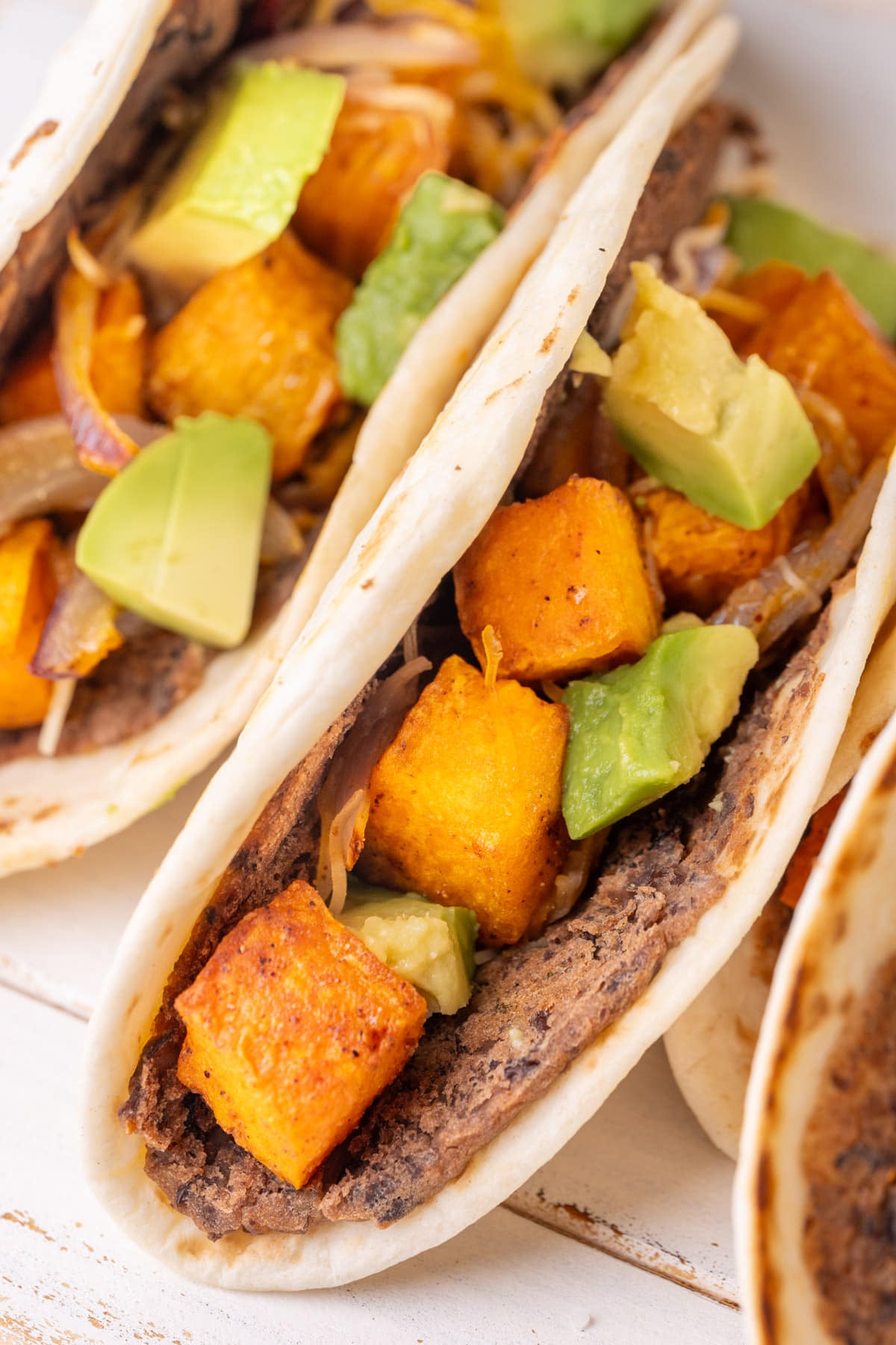 Close up of smashed black bean tacos filled with roasted sweet potato, red onions, cheese, and avocado.