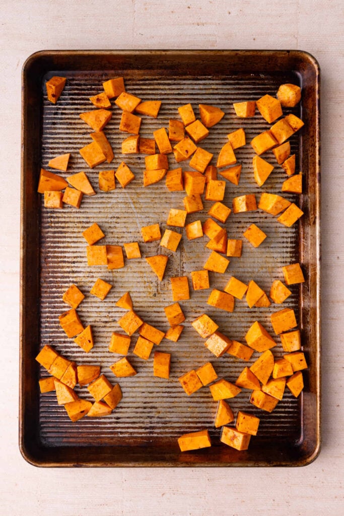 Cubed sweet potato tossed with olive oil and taco seasoning on a sheet pan.