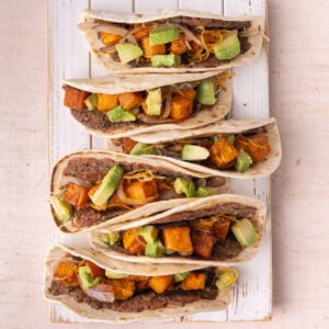 Smashed Black Bean Sweet Potato Tacos lined up on a white board.