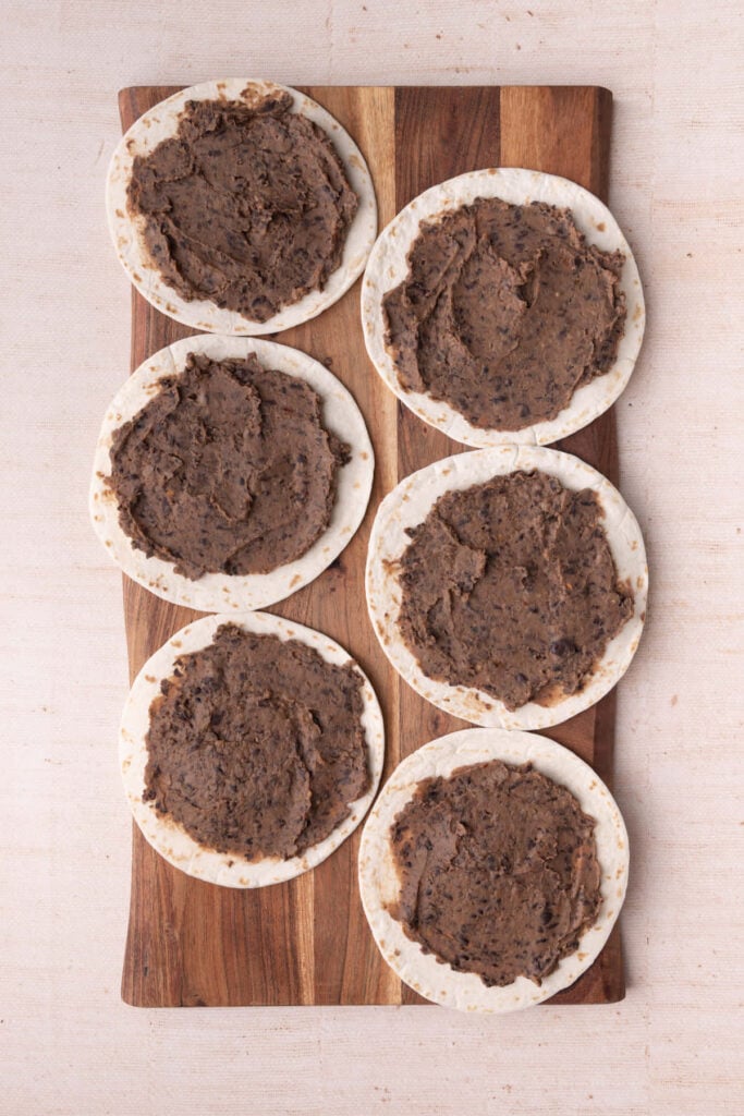 Smashed seasoned black beans spread over tortillas.