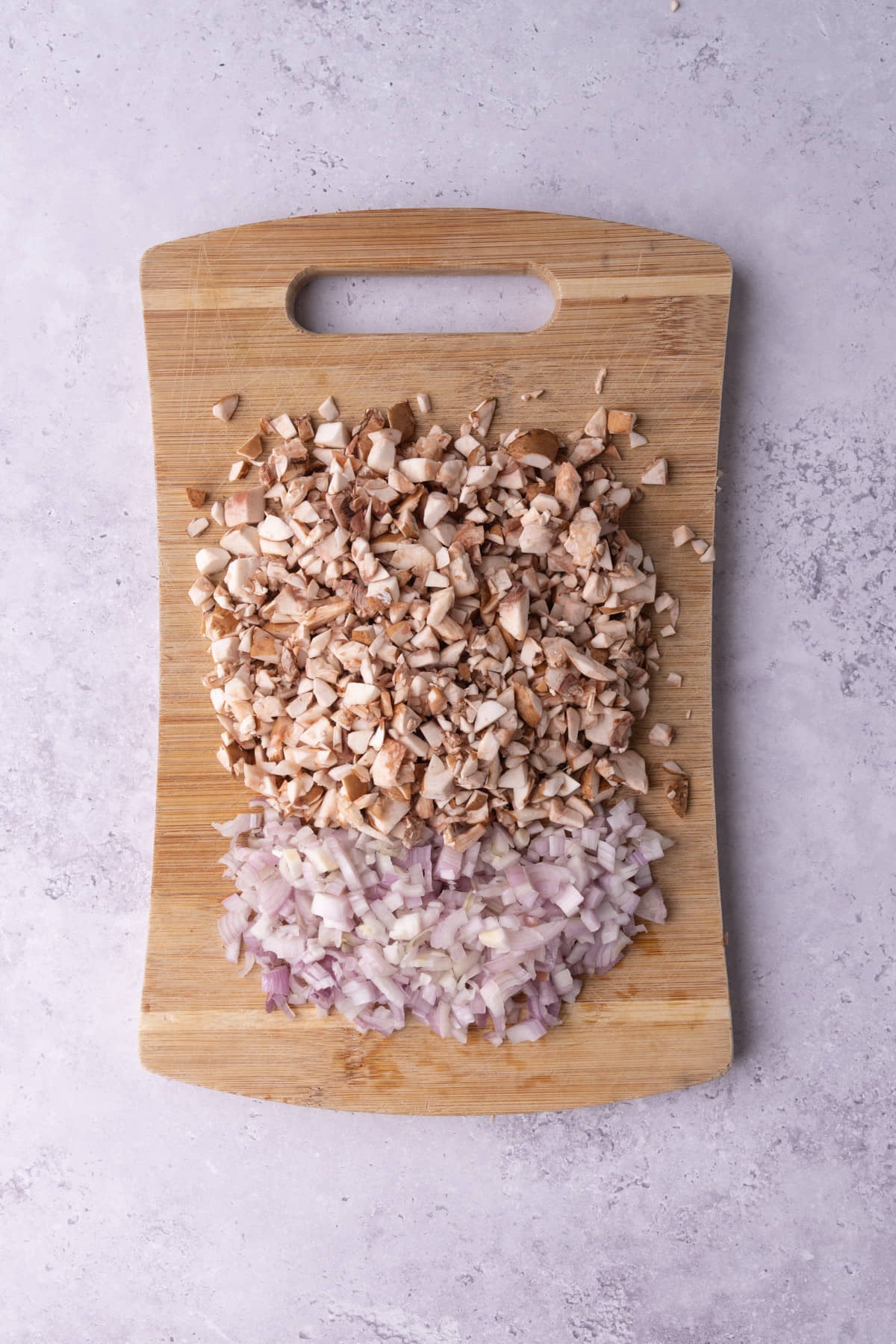 Diced mushroom and shallot on a wooden cutting board.