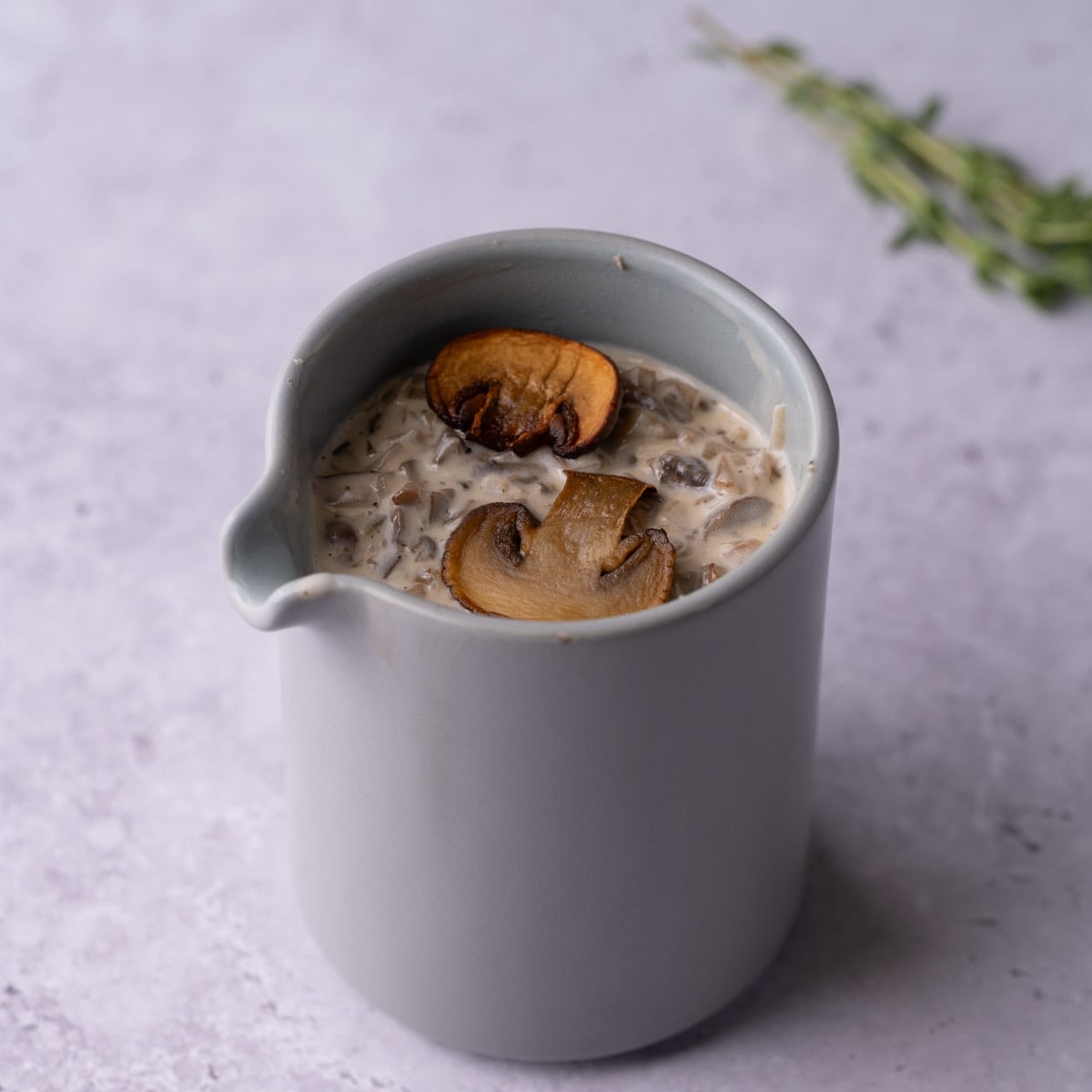 White Wine Mushroom Cream Sauce Featured Image Creamy mushroom white wine sauce in a creamer with two mushrooms floating on top.
