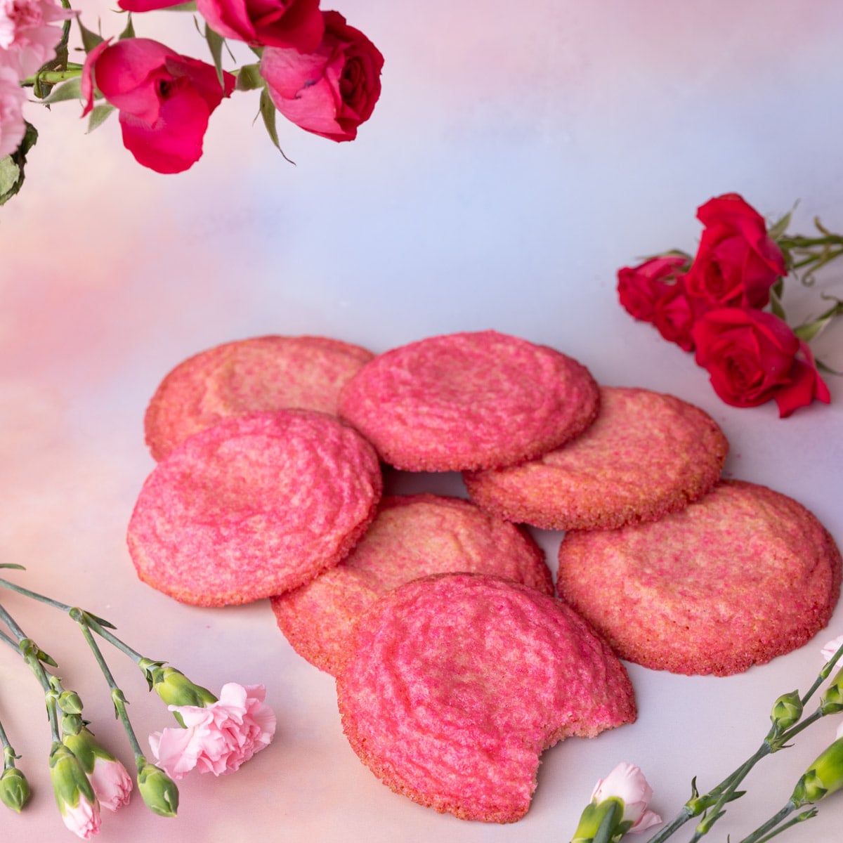 Pink sugar cookies stacked on top of one another surrounded by pink flowers.