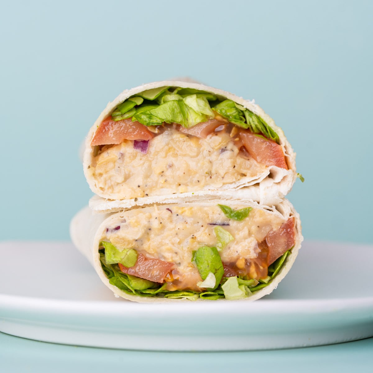 Cold chickpea wrap sliced in half and presented on a white plate with two halves stacked on top of one another.