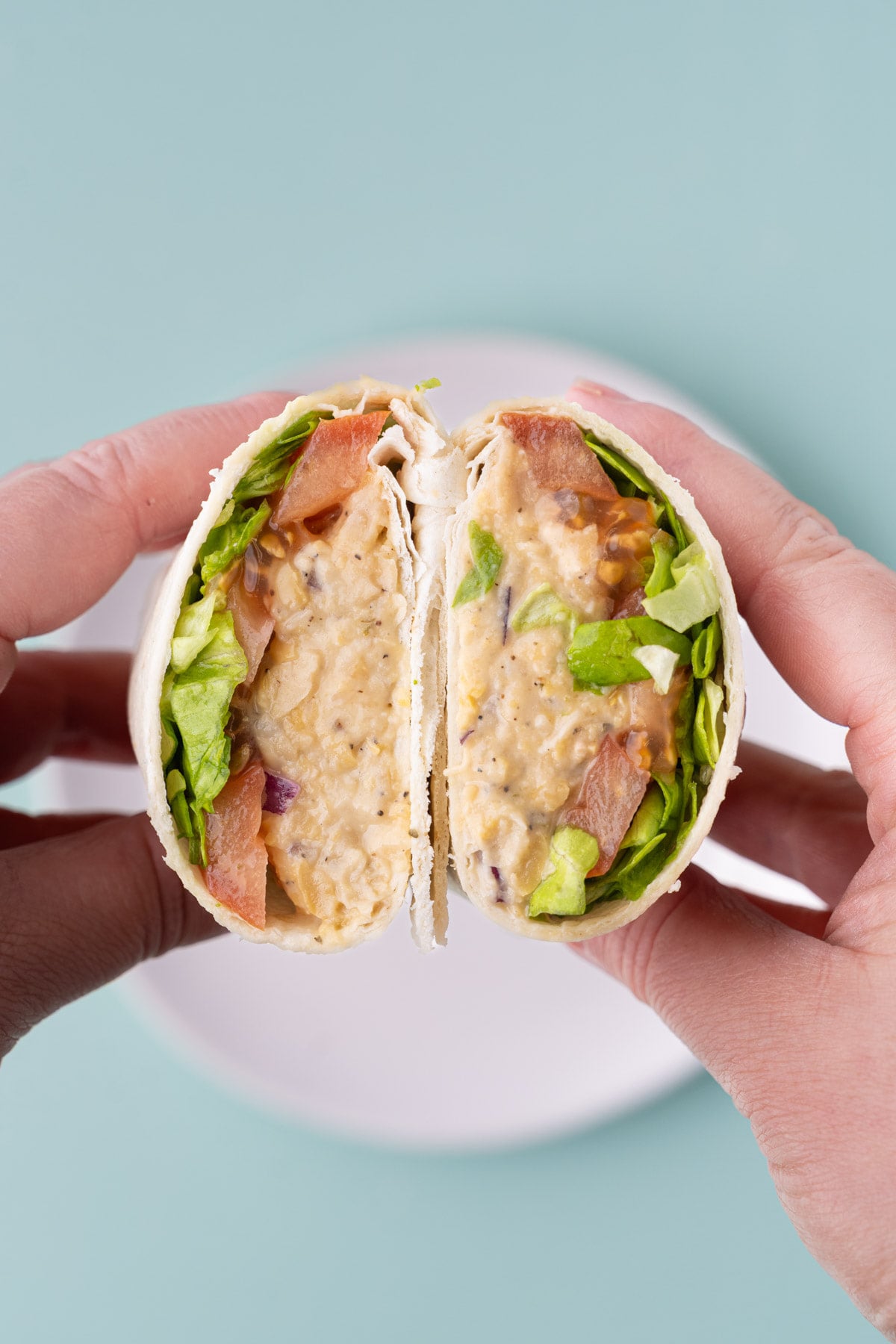 Lunch wrap with chickpea salad, tomatoes, and lettuce cut in half and held up to the camera to show the inside.