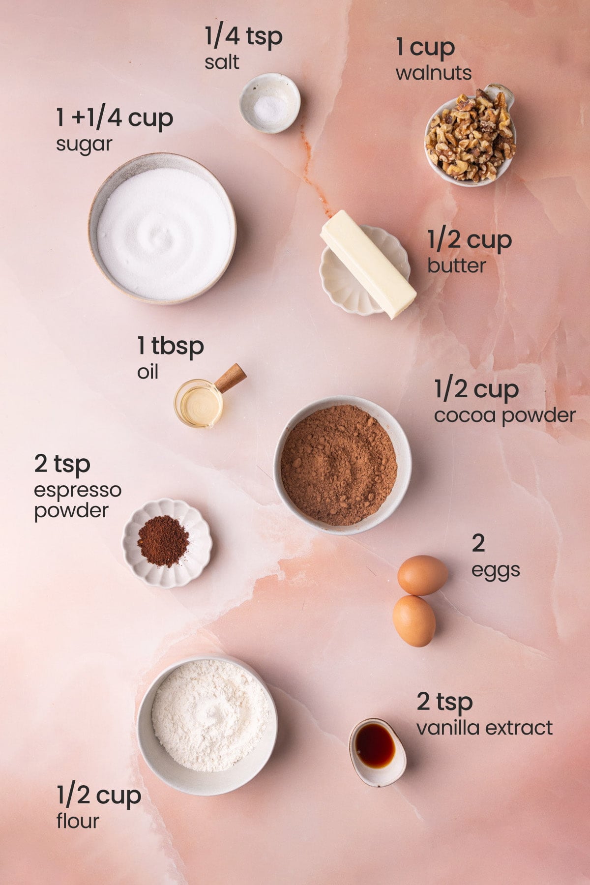 Overhead view of the ingredients needed for walnut brownies - salt, sugar, walnuts, butter, oil, cocoa powder, espresso powder, eggs, flour, and vanilla extract.