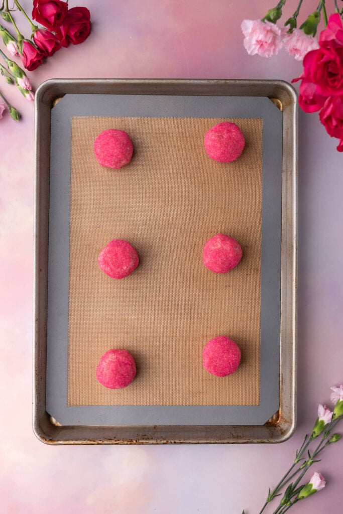 Sugar cookies coated in pink sanding sugar on a lined baking sheet ready for the oven.