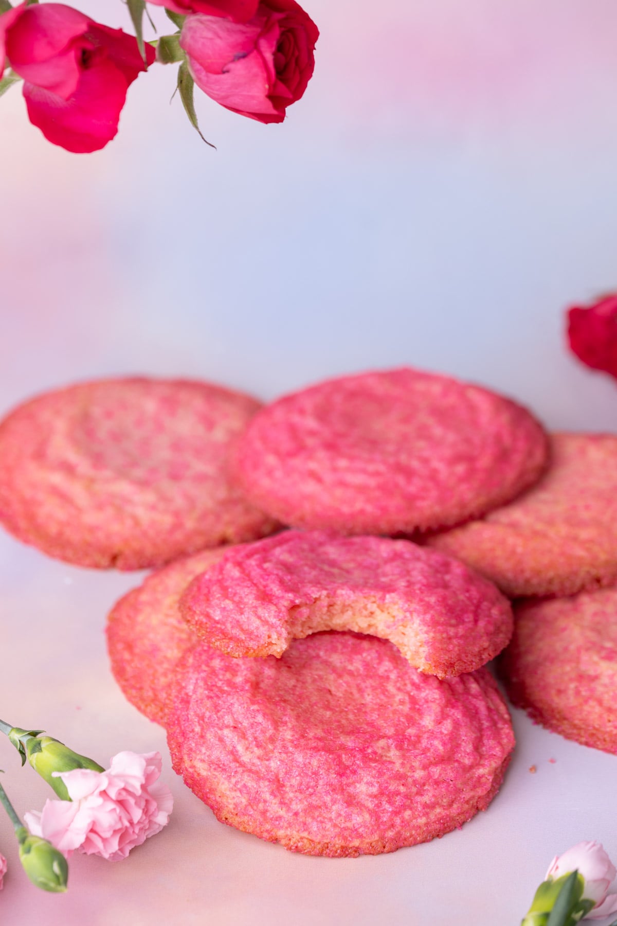 Vibrant pink sugar cookies with no frosting stacked atop one another with a bite taken out of one to show the chewy center.