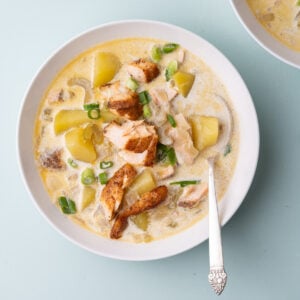 Overhead closeup image of a bowl of Salmon Chowder Soup topped with chunks of Old Bay Salmon and diced green onion.