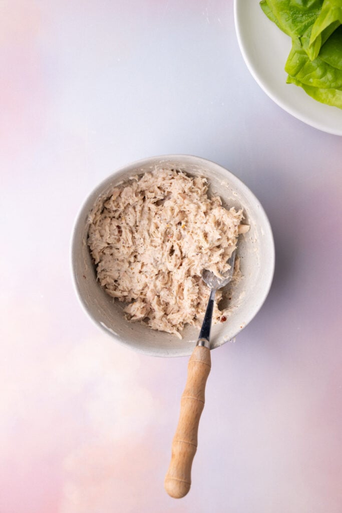 Drained canned tuna in a bowl mixed with mayonnaise and seasonings.