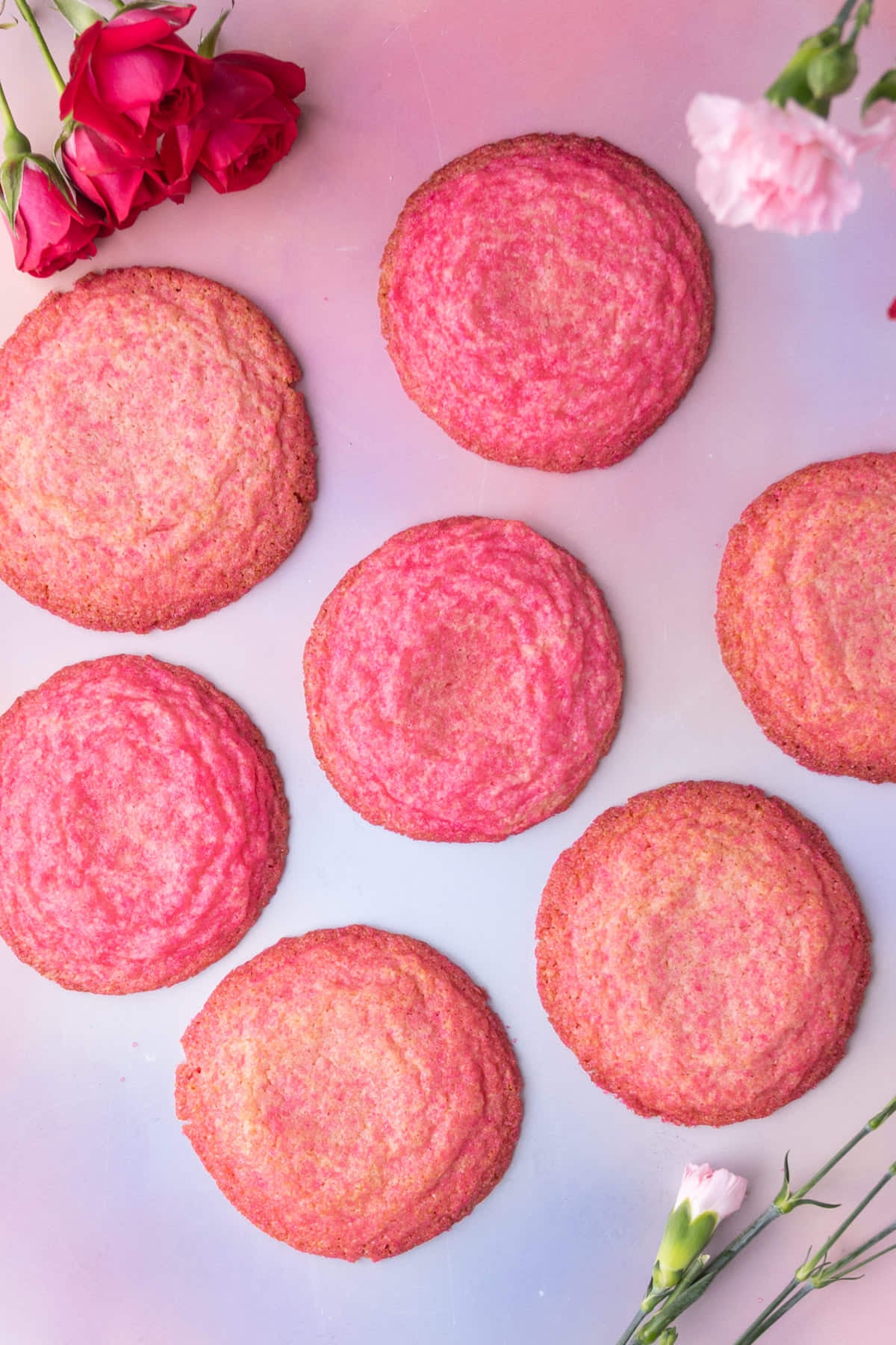 Overhead image of 7 bright pink sugar cookies on a pink and blue pastel background.