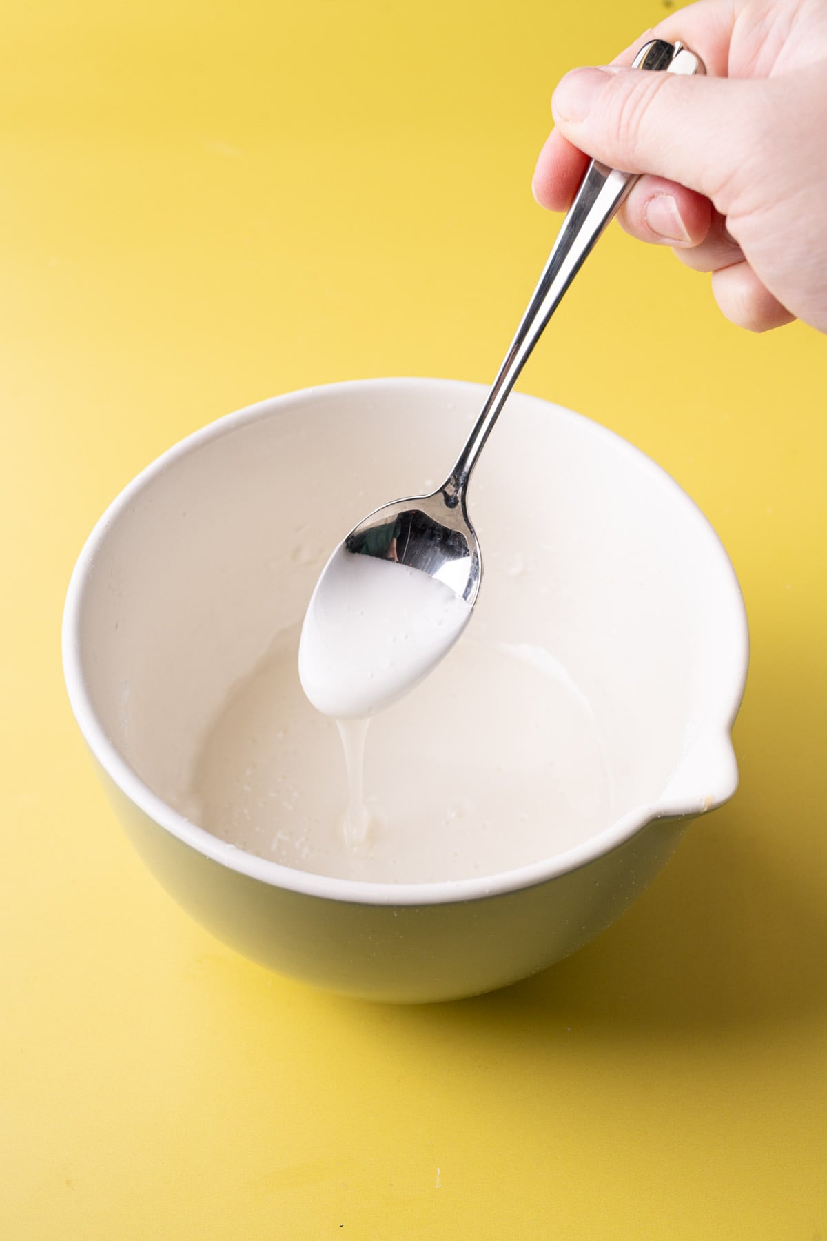 Using a spoon to check the consistency of lemon glaze made by mixing powdered sugar and lemon juice together.