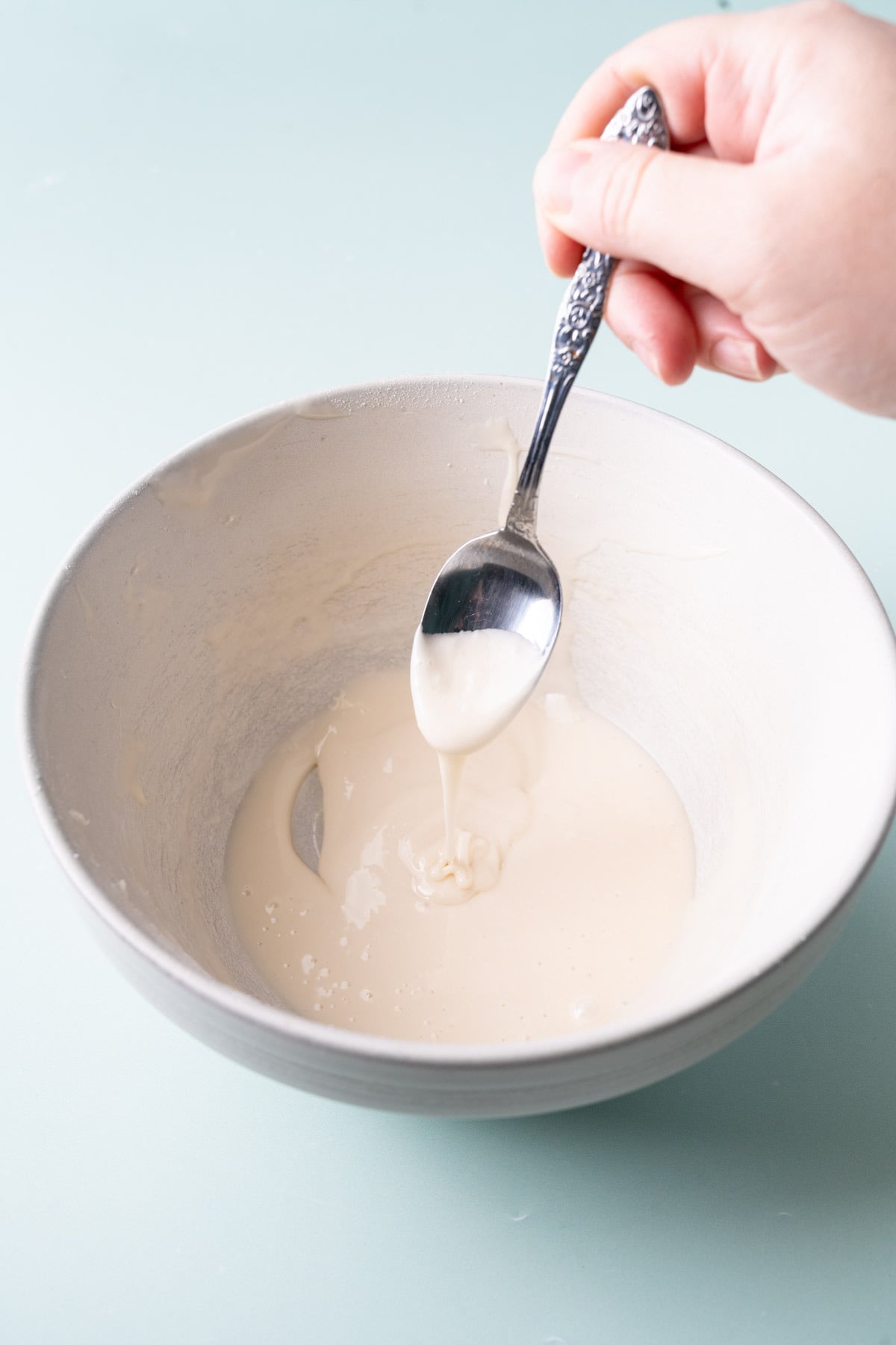 Powdered sugar mixed with milk and vanilla extract in a mixing bowl to make a simple icing, running off the spoon to check the consistency and see if any more milk is needed.