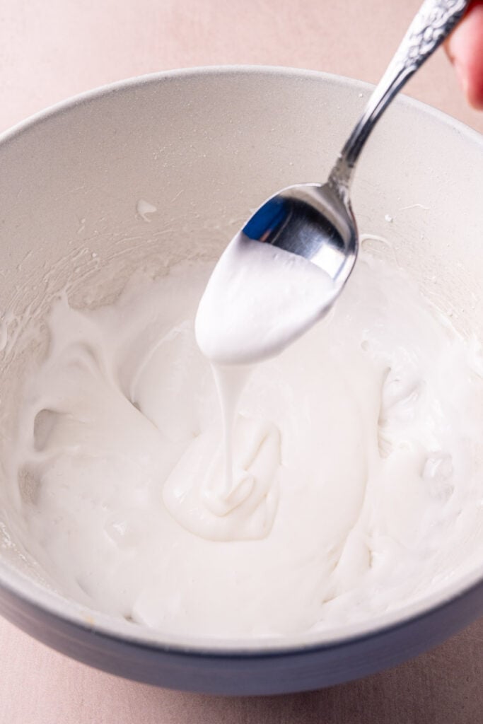 Letting coconut glaze run off a spoon to assess the consistency to know whether or not to add more coconut milk.