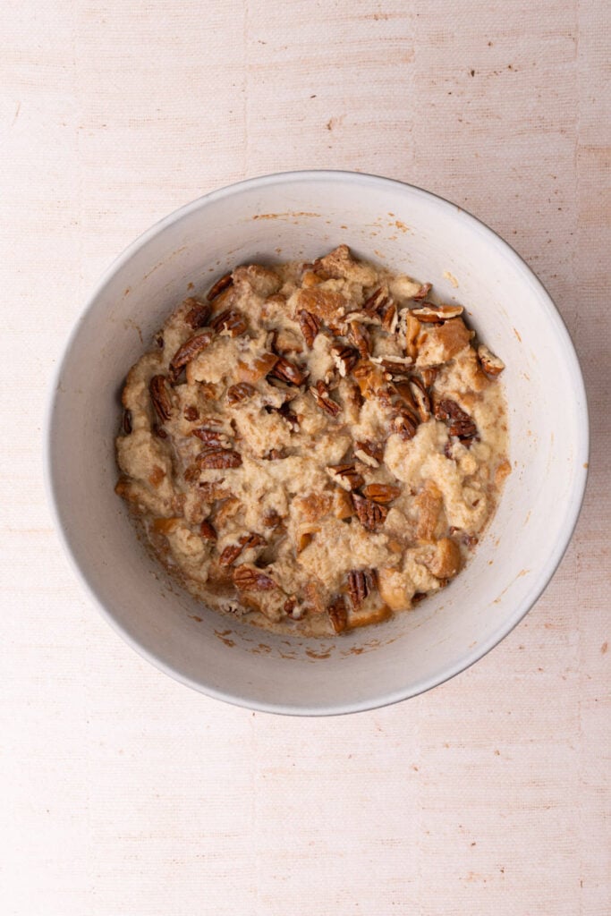 Cubed bread coated in milk-based mixture and chopped pecans.