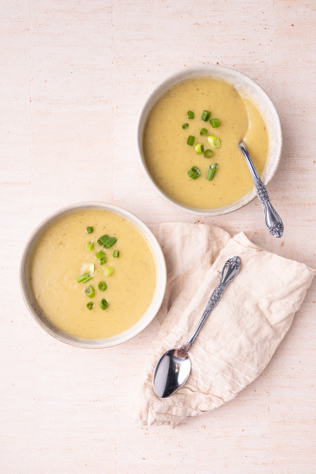 Two bowls of creamy and smooth leek and potato soup garnished with green onion.