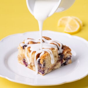 Lemon icing being poured over a piece of blueberry coffee cake.
