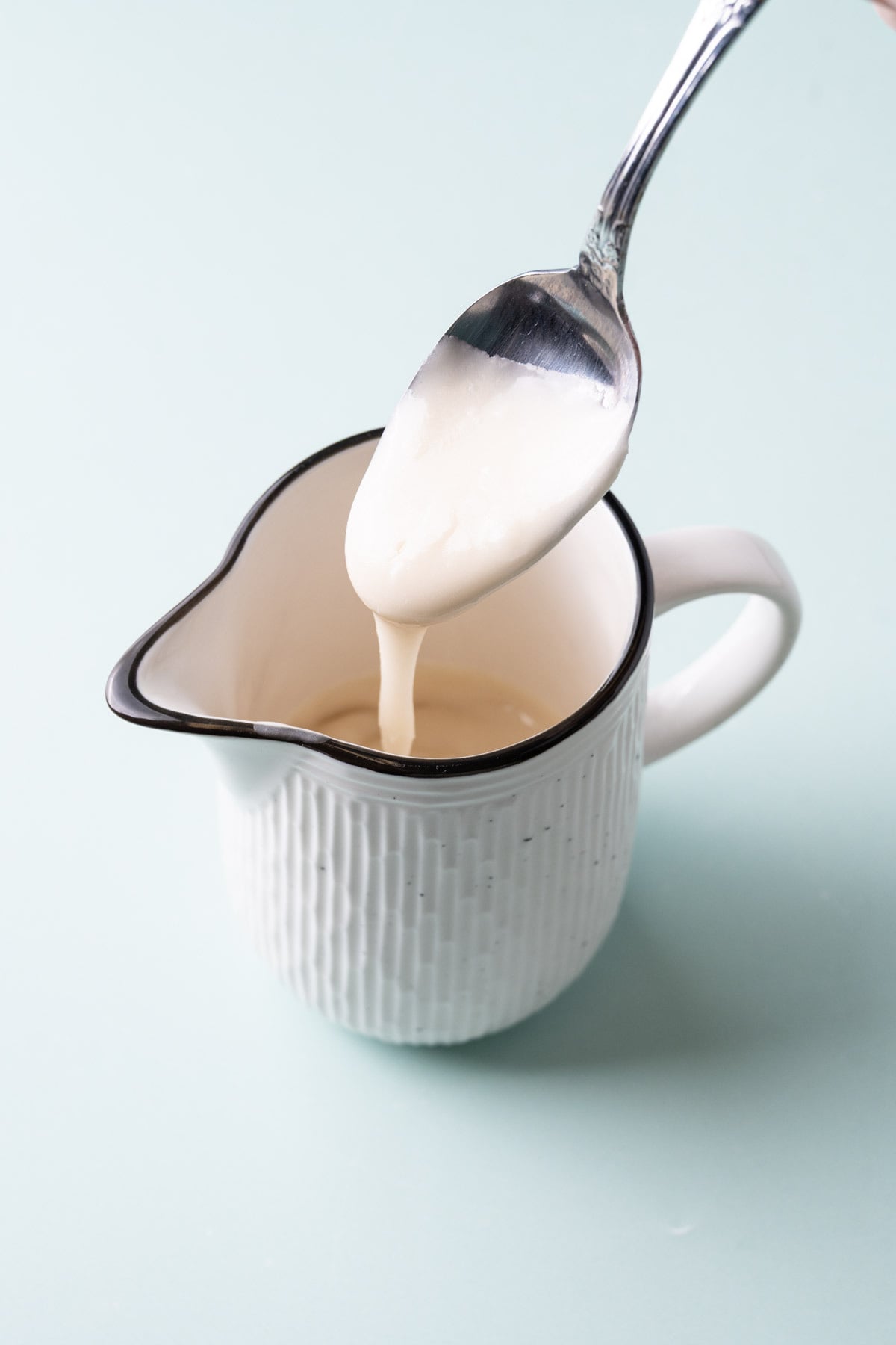 Powdered Sugar Icing dripping off a spoon into a little creamer cup to pour over pound cake, coffee cake, cookies, and more!