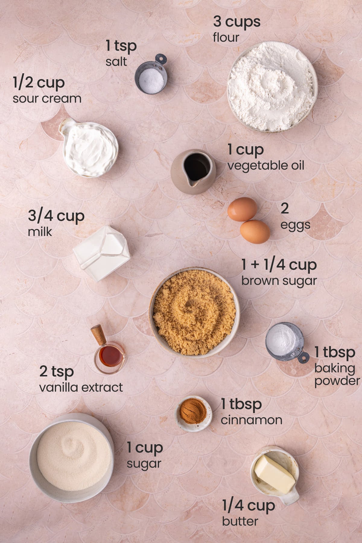 All ingredients needed for sour cream coffee cake including salt, flour, sour cream, oil, eggs, milk, brown sugar, baking powder, vanilla extract, cinnamon, granulated sugar, and butter.