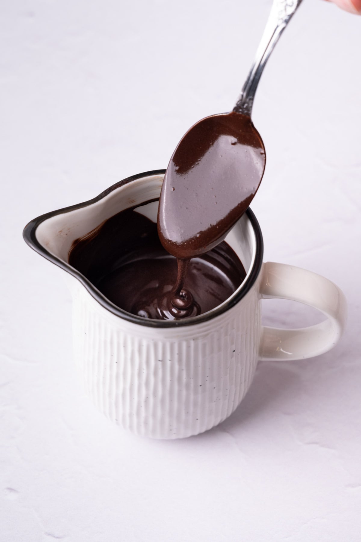 Pourable chocolate glaze running off a spoon into a creamer.