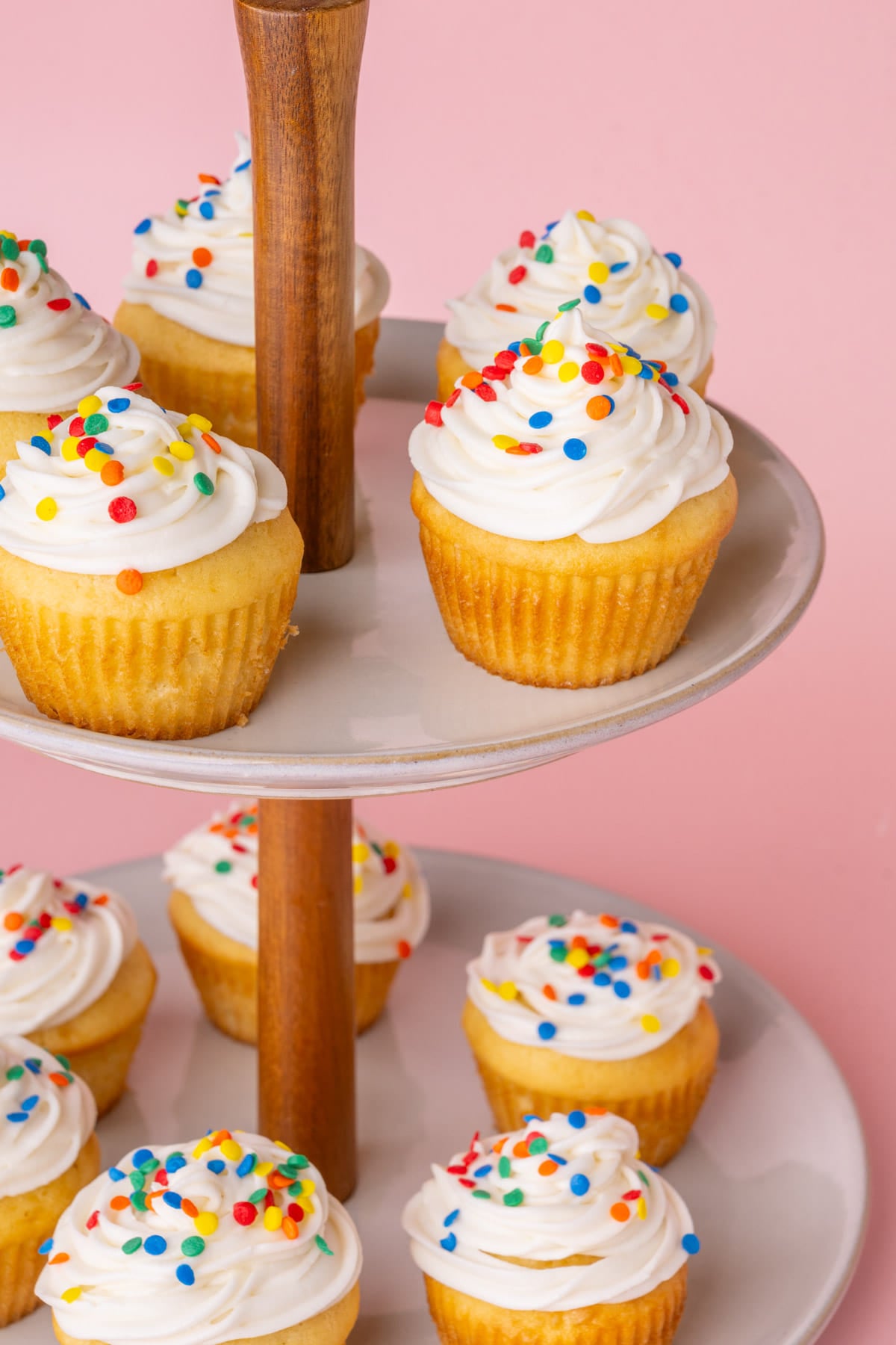 Two-tiered cupcake display with vanilla cupcakes with a generous amount of sour cream frosting piped on each.