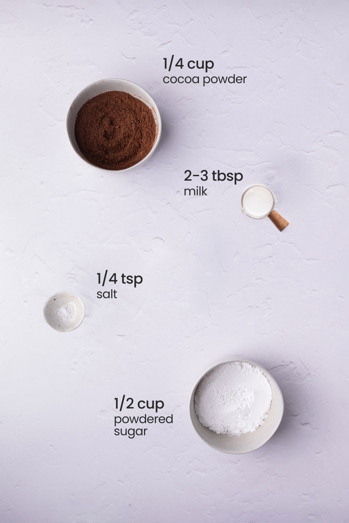 Overhead view of the ingredients needed for pourable chocolate glaze - cocoa powder, milk, salt, and powdered sugar.