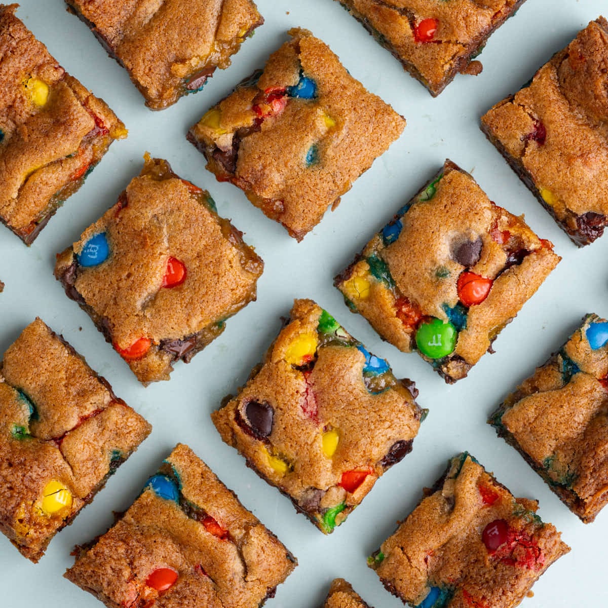 M&M Cookie Bars on Blue Background Overhead image of M&M cookie bars sliced into squares on a blue background.