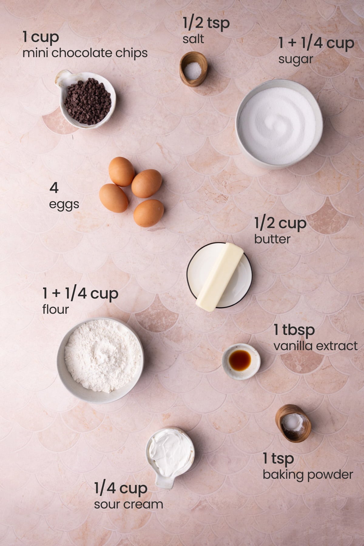 Overhead view of the ingredients needed for chocolate chip pound cake - mini chocolate chips, salt, sugar, eggs, butter, flour, vanilla extract, sour cream, and baking powder.