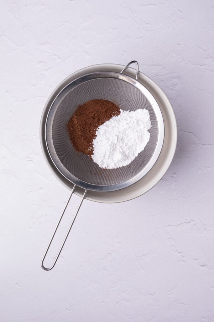 Sifting cocoa powder and powdered sugar into a large mixing bowl.