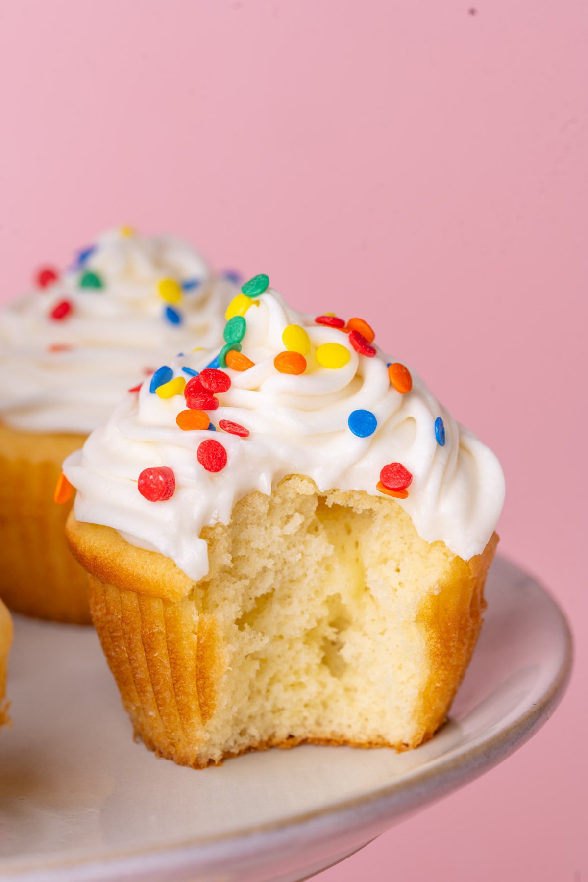 Vanilla cupcake with light and airy frosting made with sour cream with a bite taken out of it.