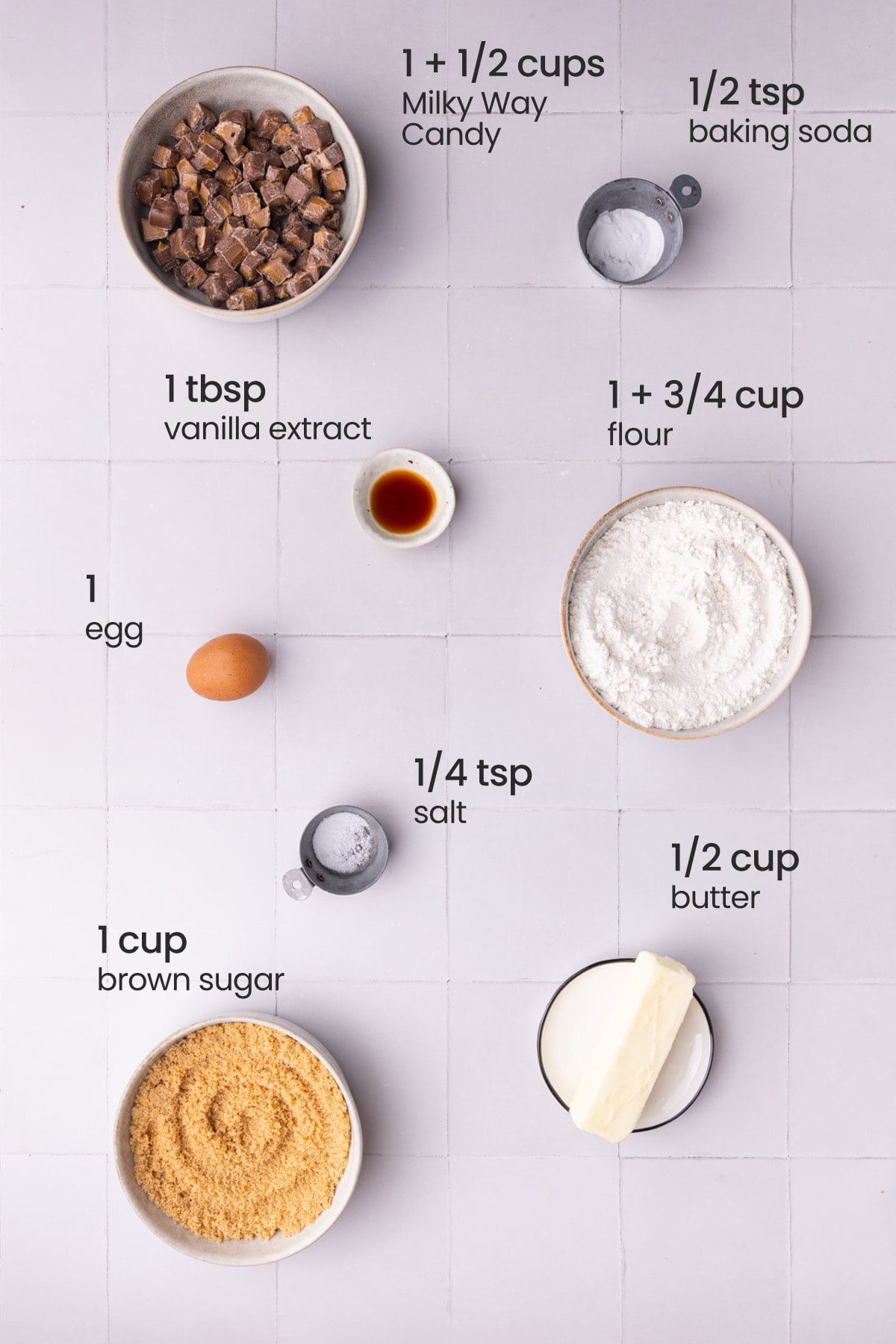 Overhead view of the ingredients needed for Milky Way Cookies - Milky Way candy bards, baking soda, vanilla extract, flour, egg, salt, butter, and brown sugar.