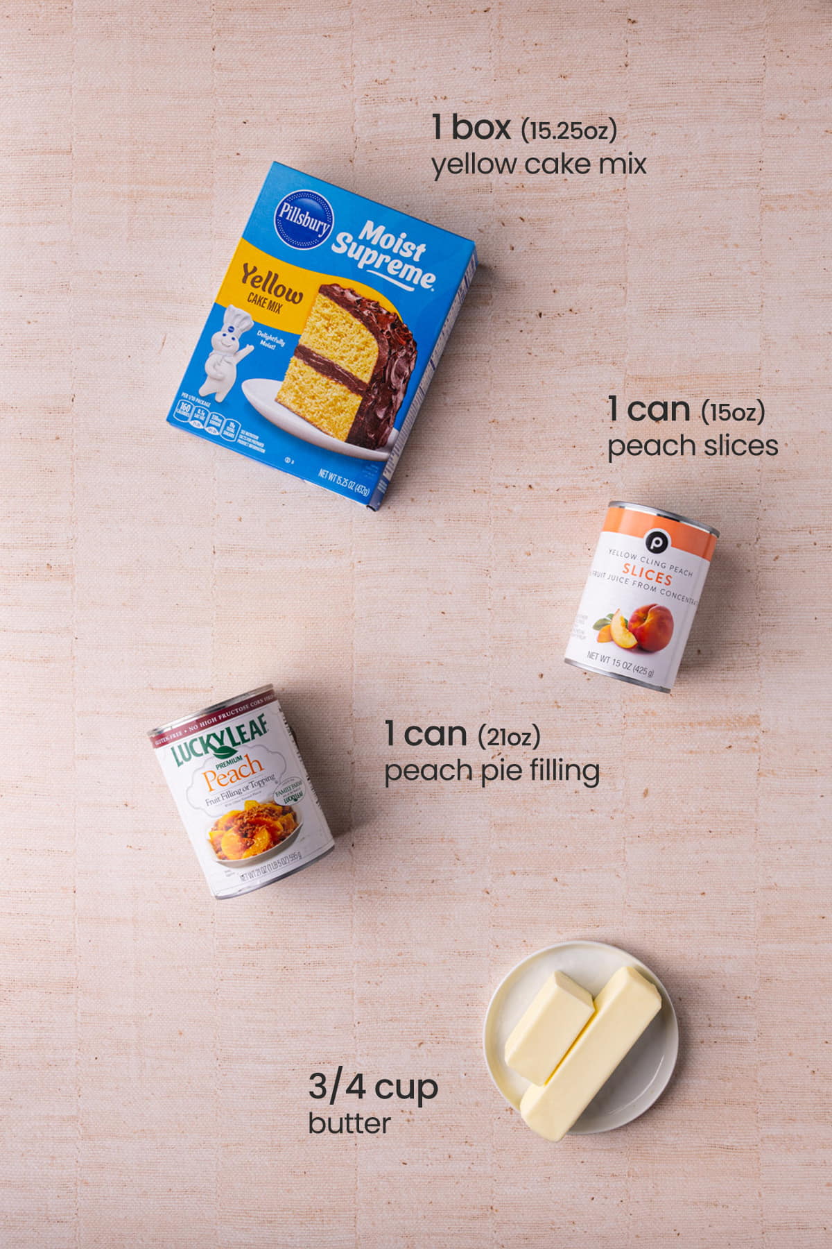 Overhead view of the ingredients needed for 4-ingredient peach cake - yellow cake mix, peach slices, peach pie filling, and butter.