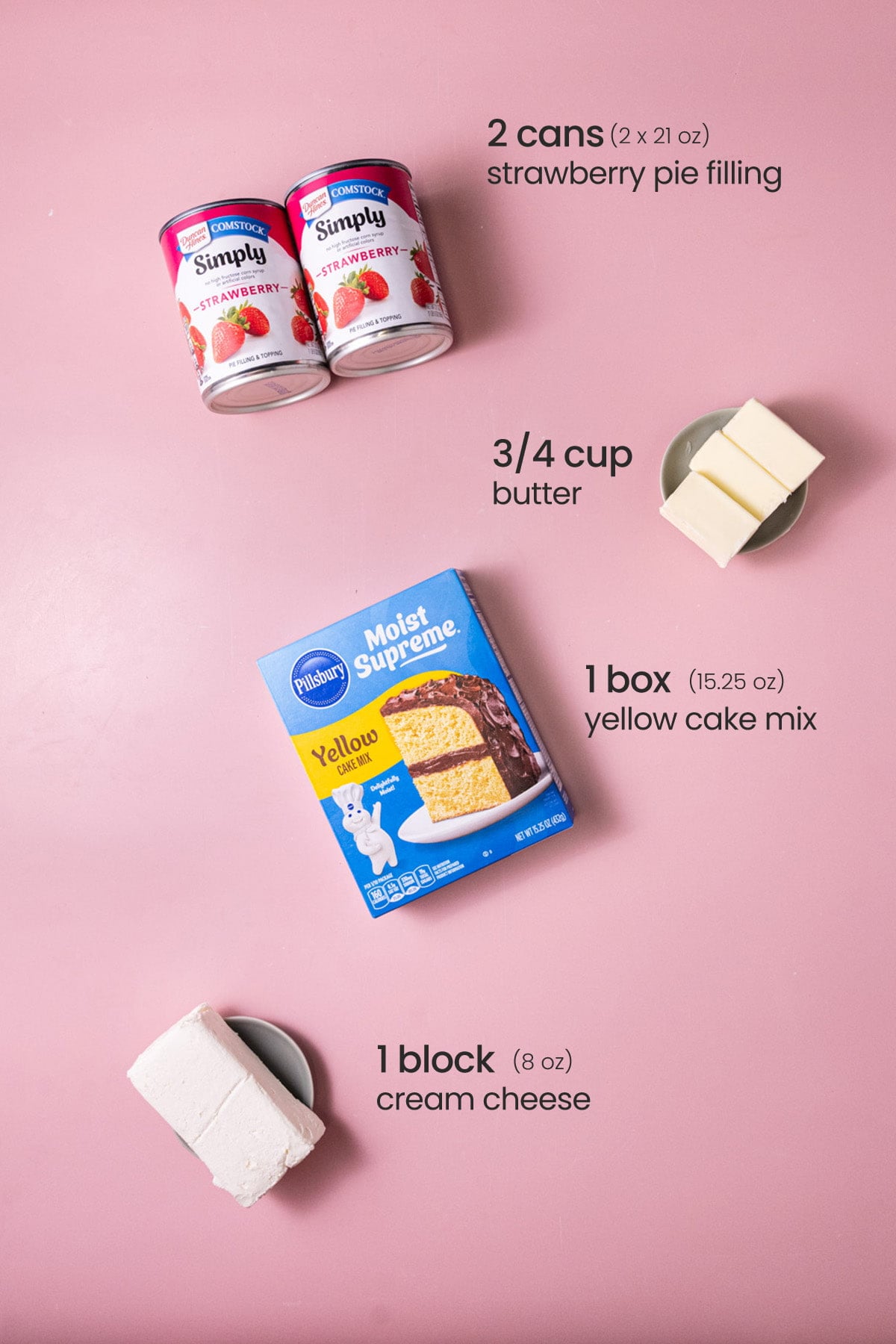 Overhead view of the ingredients needed for strawberry cheesecake dump cake - strawberry pie filling, butter, yellow cake mix, and cream cheese.