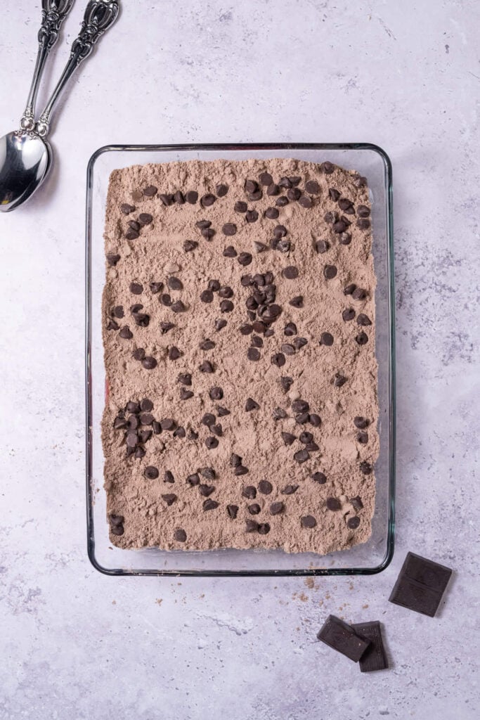 Casserole dish with chocolate box cake mix sprinkled on top of cherry pie filling and topped with chocolate chips.