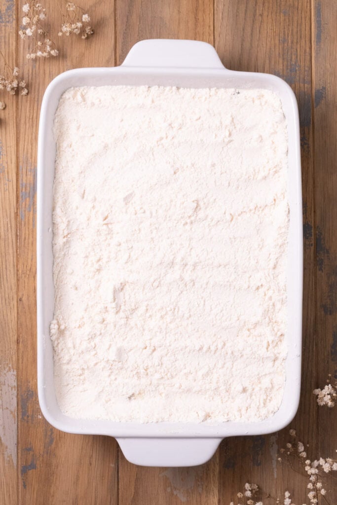 Box yellow cake mix in single layer covering apple pie filling in a casserole dish.