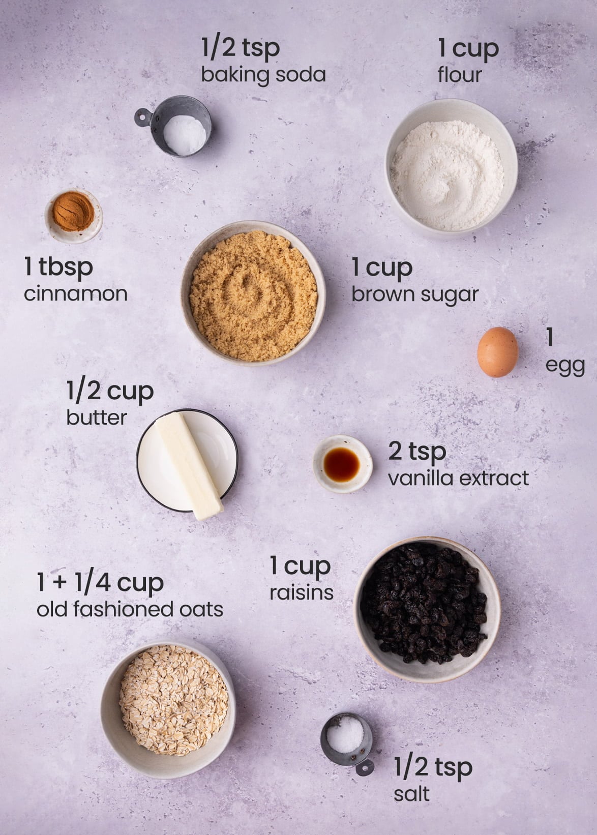 Overhead view of the ingredients needed for Chewy Oatmeal Cookie Bars with Raisins - baking soda, flour, cinnamon, brown sugar, butter, egg, vanilla extract, old fashioned oats, raisins, and salt.