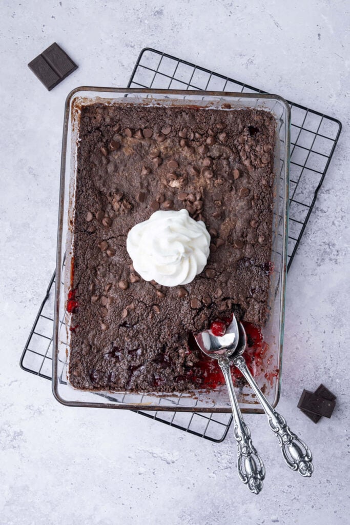 Overhead image of cherry chocolate dump cake with portion scooped out and whipped cream in the center.