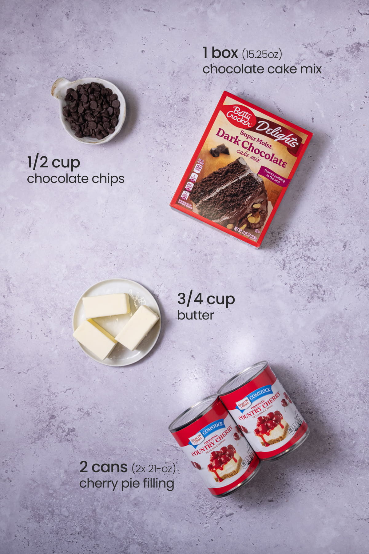 Overhead view of the ingredients needed for chocolate cherry dump cake - chocolate chips, chocolate cake mix, butter, and cherry pie filling.