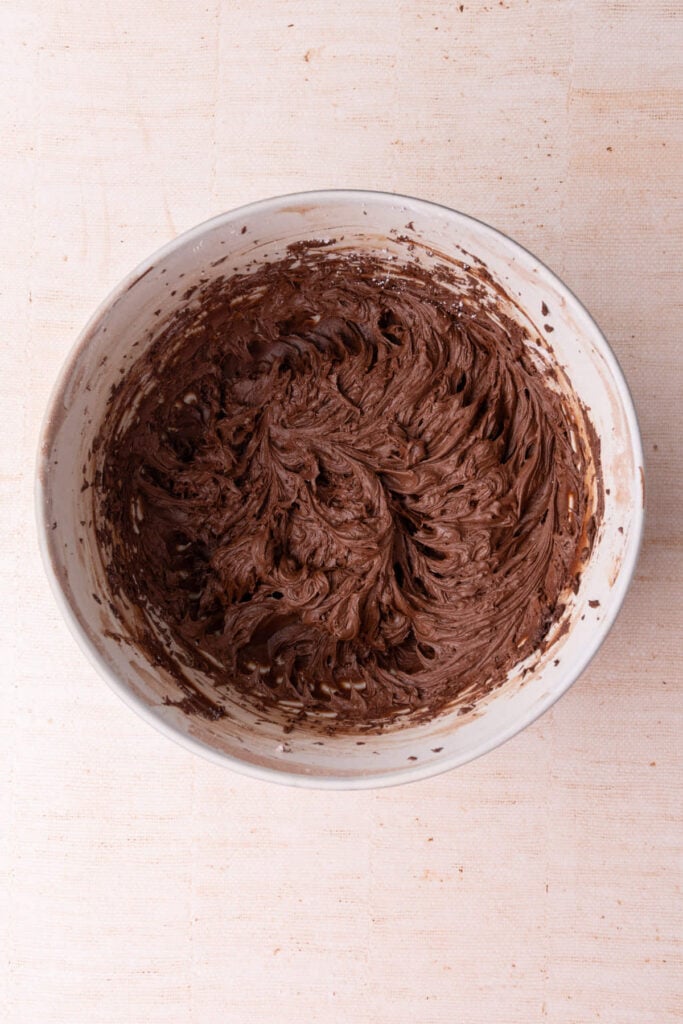 Thick chocolate fudge frosting freshly made in a large mixing bowl ready to pipe or spread.