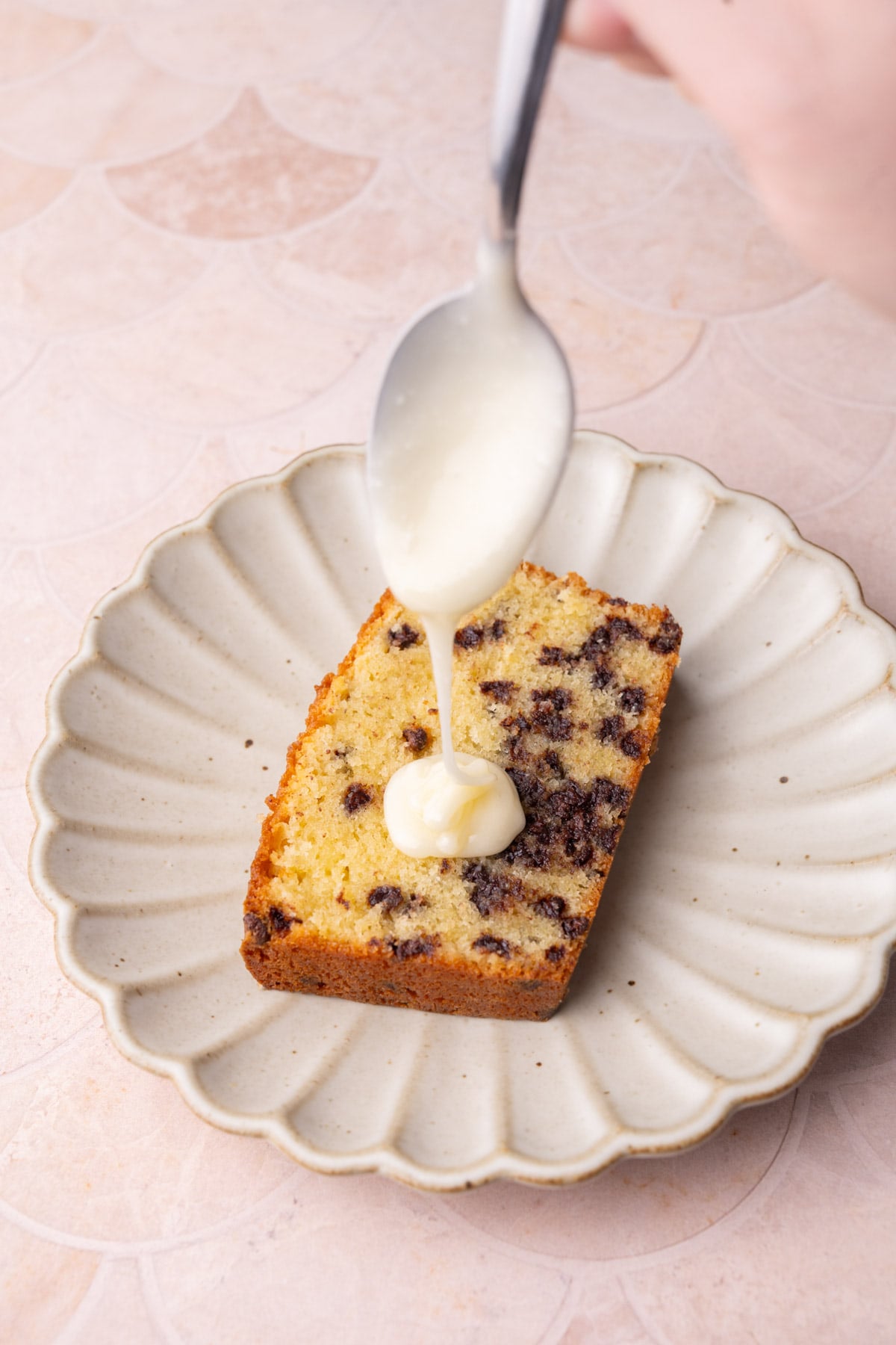 White chocolate glaze running off a spoon onto a slice of chocolate chip pound cake.