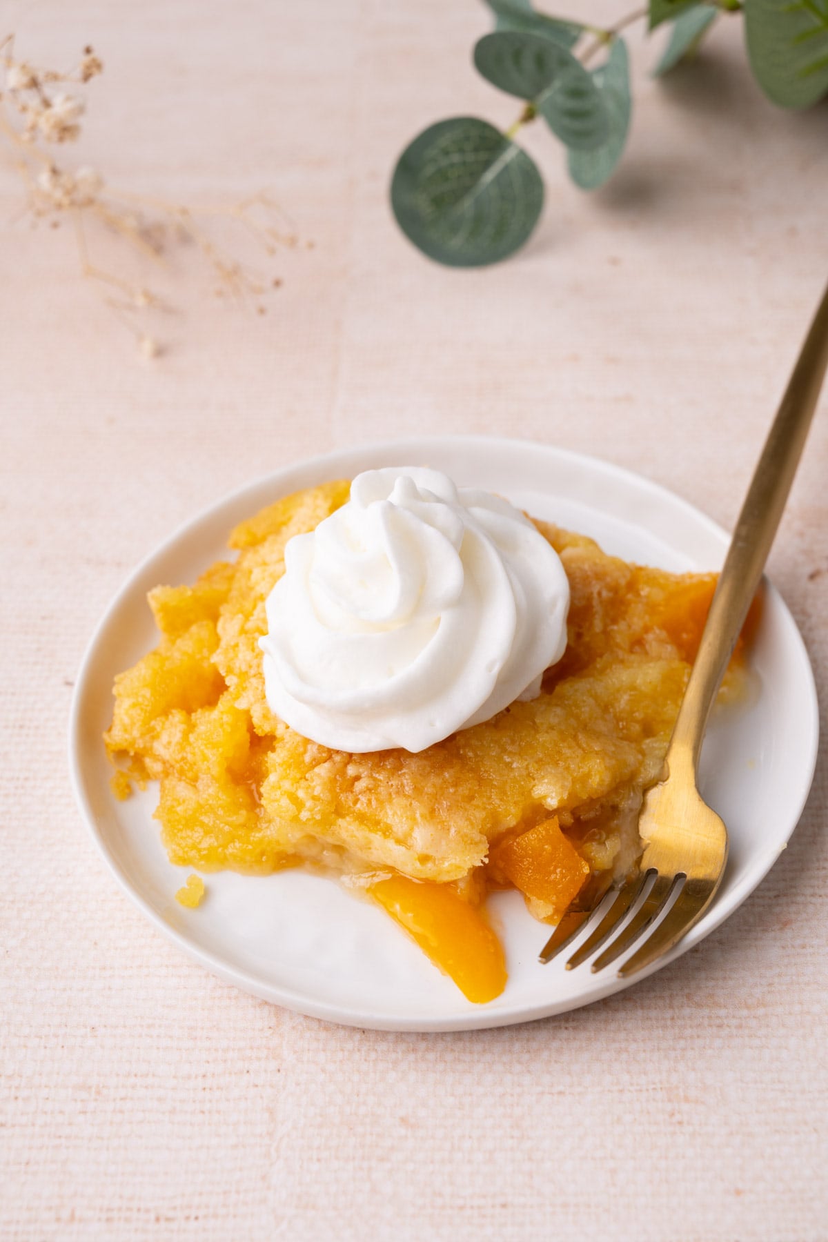 Plate with portion of peach dump cake topped with whipped cream.