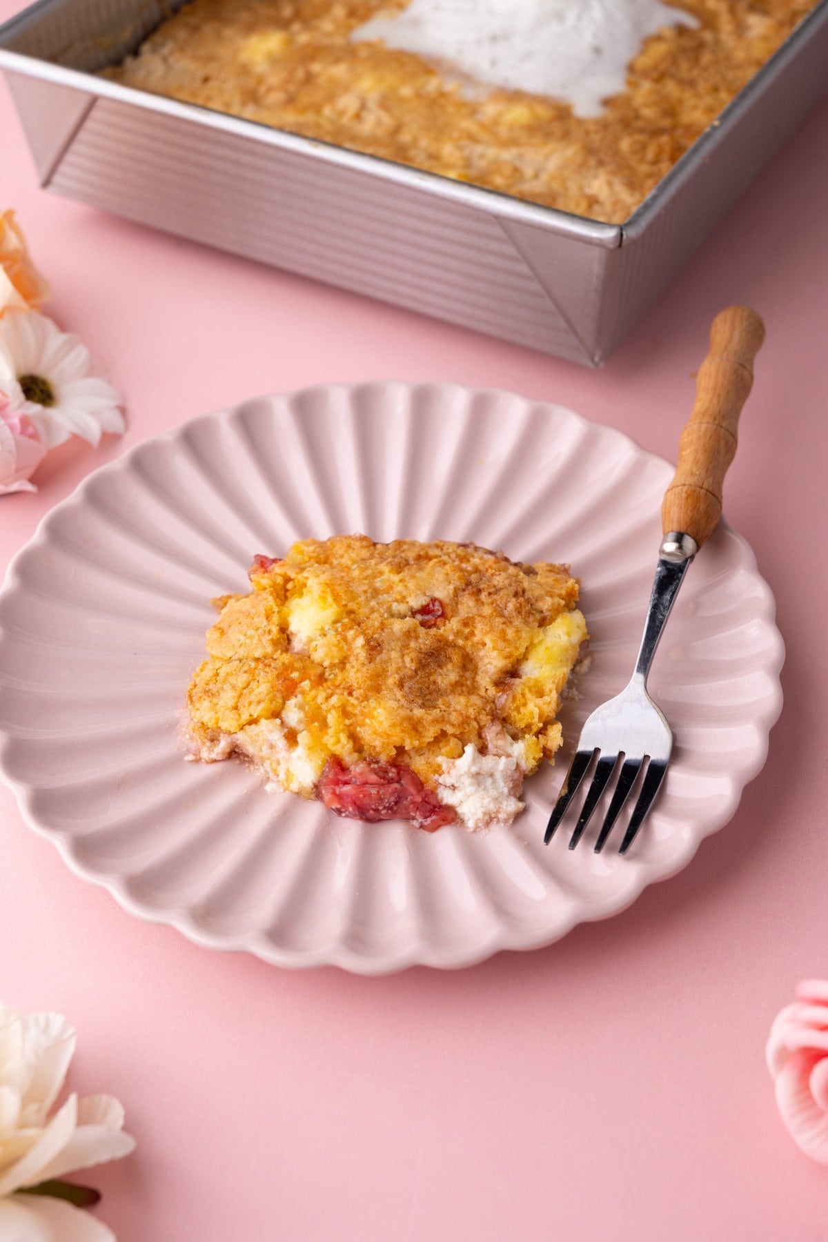 Serving of Strawberry Cheesecake Dump Cake on a pink scalloped plate with a fork.