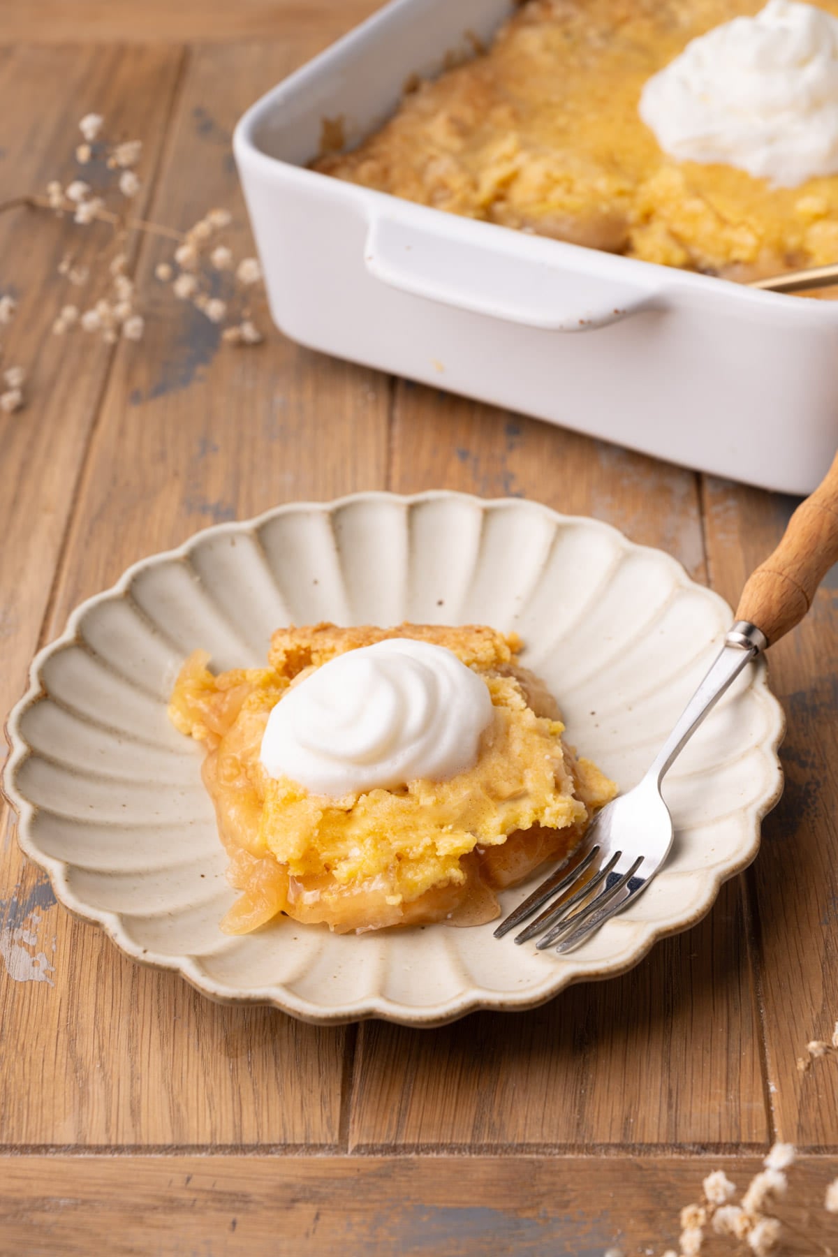 Serving of apple dump cake on a scalloped plate with whipped cream on top.