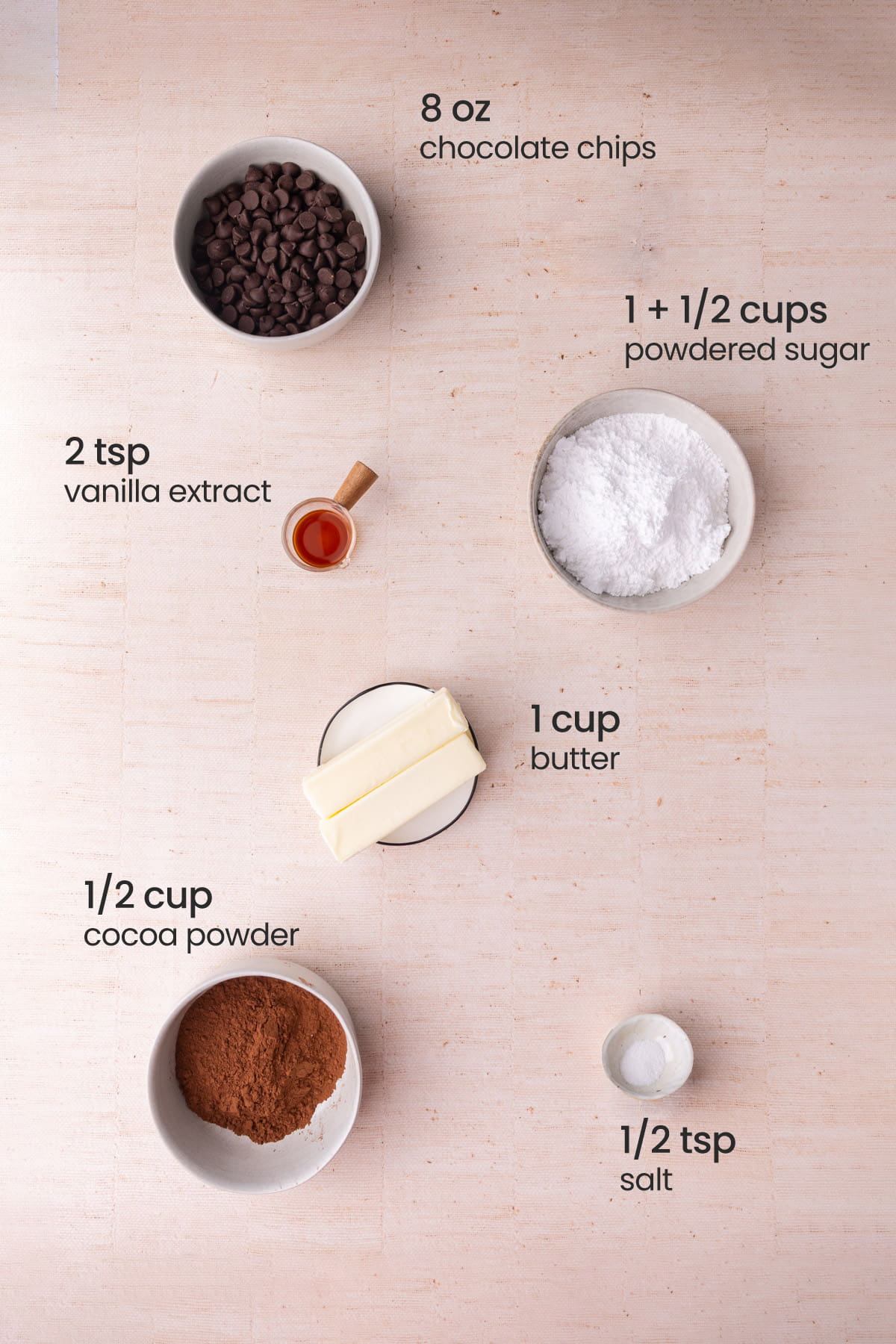 Overhead view of the ingredients needed for chocolate fudge frosting - chocolate chips, vanilla extract, powdered sugar, butter, cocoa powder, and salt.