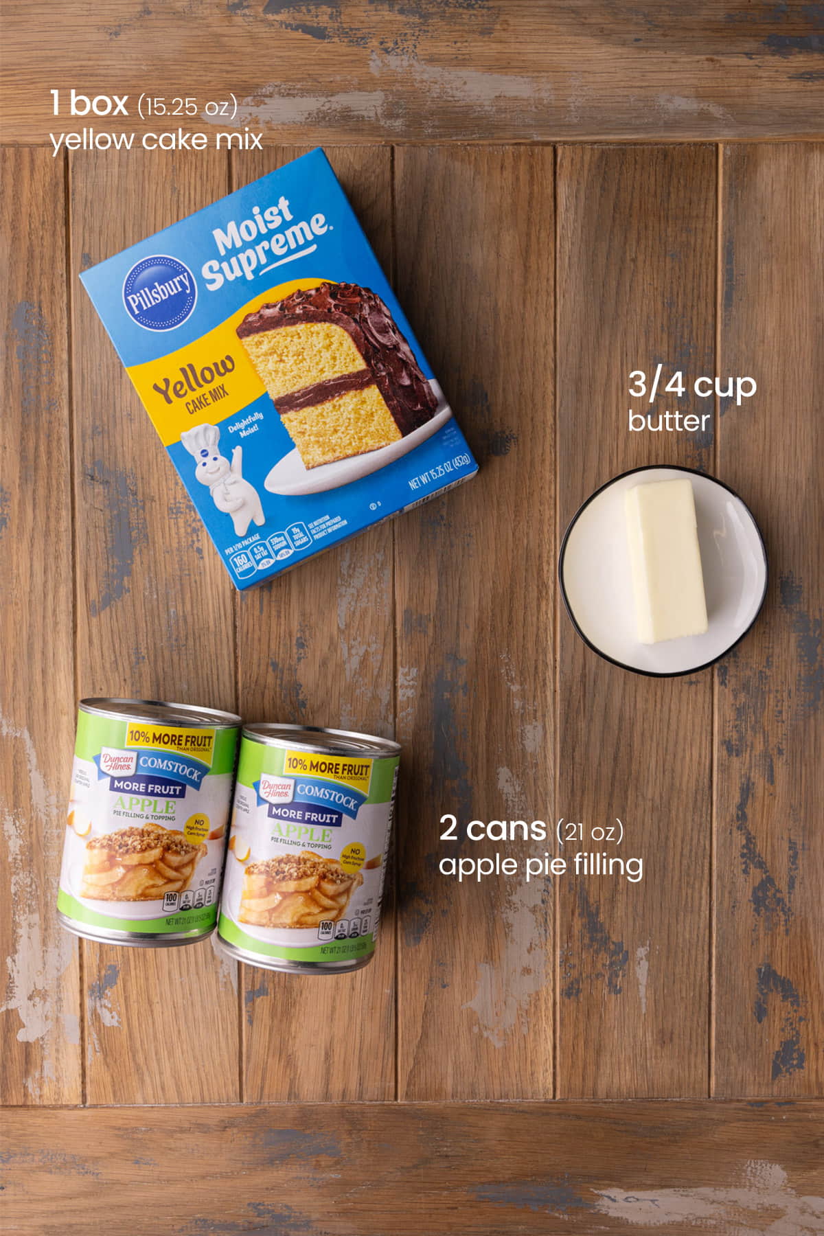 Overhead view of the ingredients for dump and bake apple cake - yellow cake mix, butter, and apple pie filling.