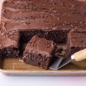 Taking a serving of chocolate poke cake off of the baking pan, showing the super-moist texture on the inside.